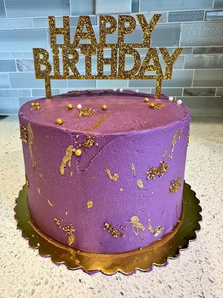 Tall purple cake with gold flecks and a glittery gold Happy Birthday topper