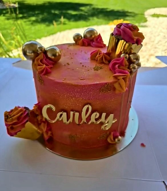 Pink and orange cake with gold spheres, bright rosettes and a gold name topper
