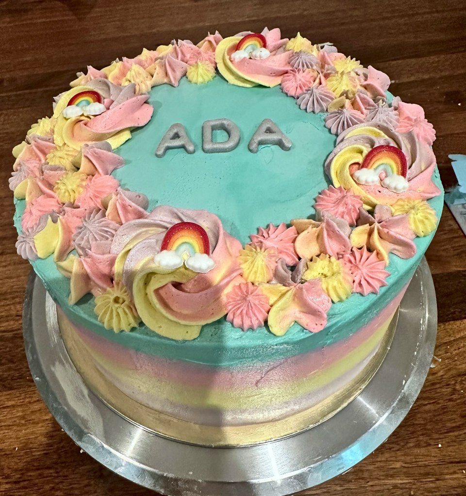 Teal cake with pastel rainbow sides, rainbow rosettes and a name on top