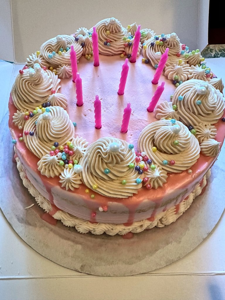 Pink and white birthday cake with frosting rosettes, sprinkles and pink candles