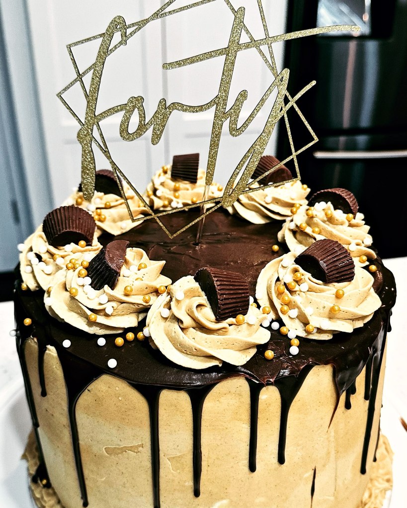 Drip cake with a chocolate drip, peanut butter cups, gold sprinkles and a gold Forty topper