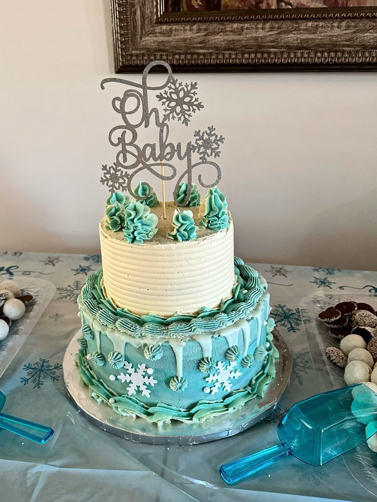 Two-tier blue and white baby shower cake with snowflakes and an Oh Baby topper