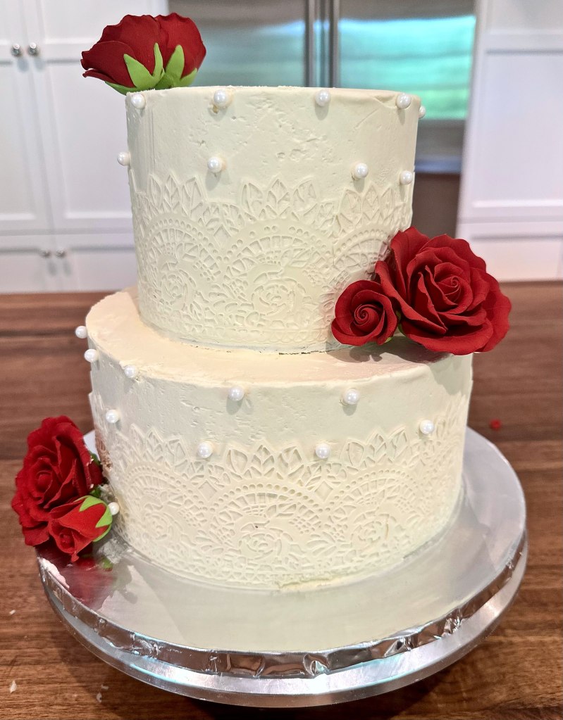 Two-tier white cake with a lace pattern and red roses