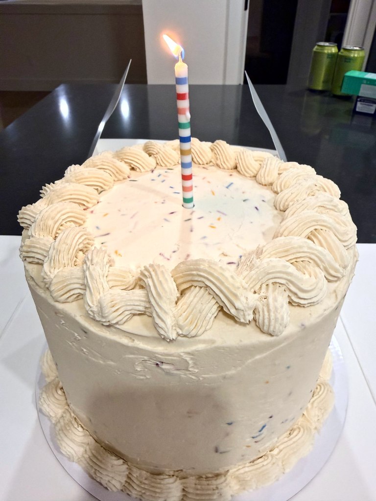 White cake flecked with colorful sprinkles, a braided frosting border and a striped birthday candle