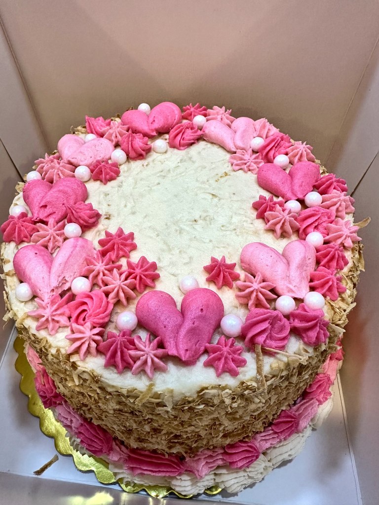 White cake covered in pink frosting hearts, stars, pearls and rosettes
