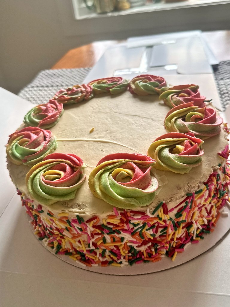Cake with rainbow swirl rosettes on top and rainbow sprinkles around the sides