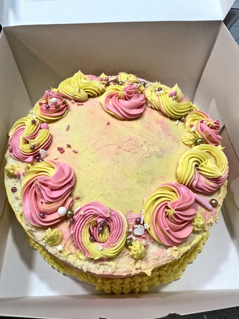 Round cake with pink, yellow and green swirled rosettes and sprinkles