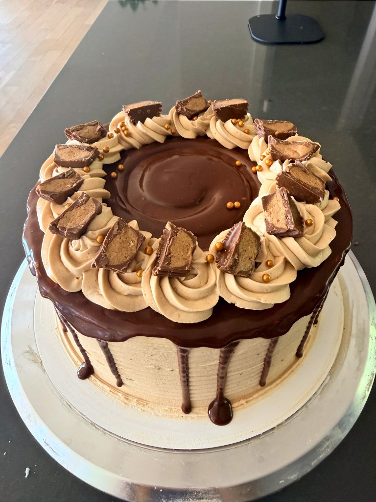 Chocolate drip cake topped with frosting swirls, cut peanut butter cups and gold pearls