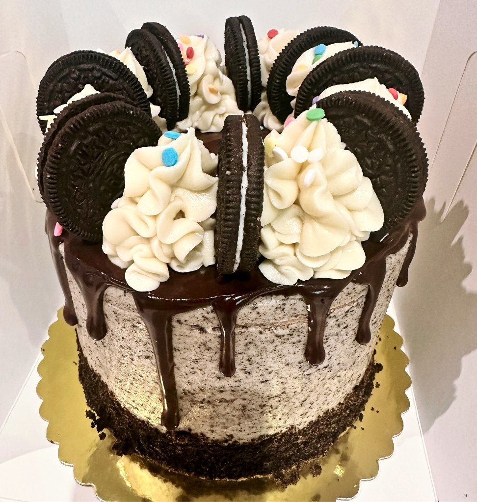 Tall cookies and cream cake with a chocolate drip, frosting swirls and whole Oreo cookies