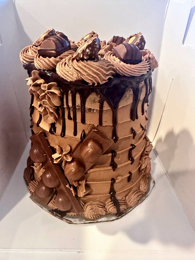 Tall chocolate cake covered in a chocolate drip, frosting swirls and chocolate candies