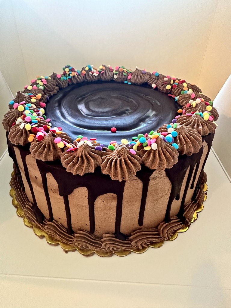Chocolate cake with a glossy top, a chocolate drip and chocolate stars with rainbow sprinkles