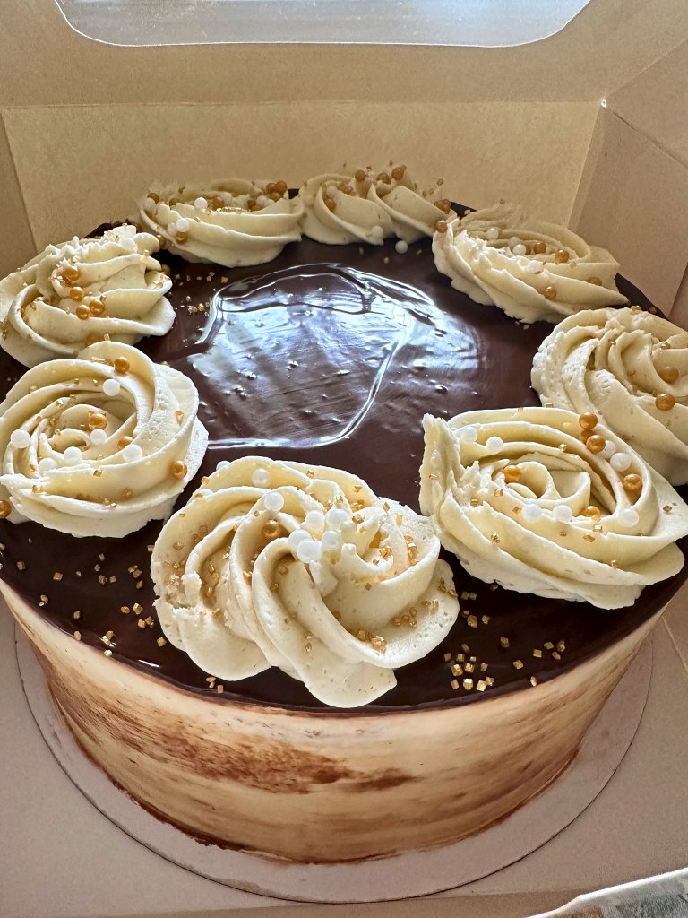 Cake with a glossy chocolate top, cream frosting rosettes and gold sprinkles
