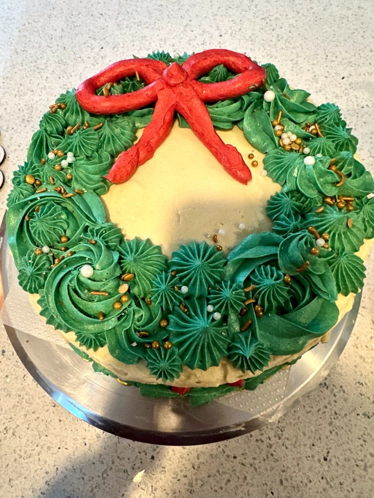 Christmas wreath cake with green frosting leaves, a red bow and gold sprinkles