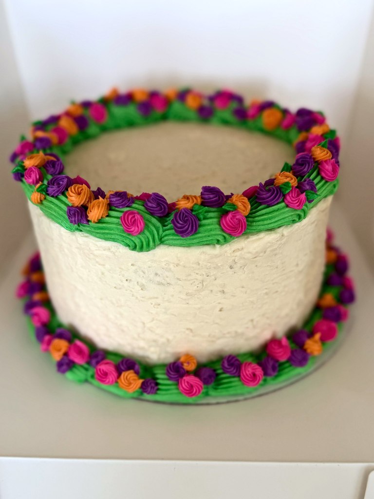White cake with bright green borders and pink, purple and orange frosting flowers
