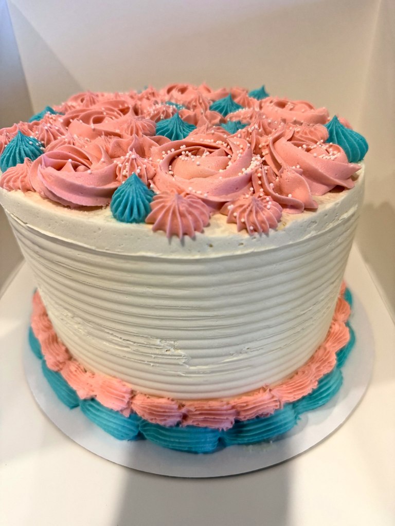 White cake with coral and teal frosting rosettes on top and around the bottom
