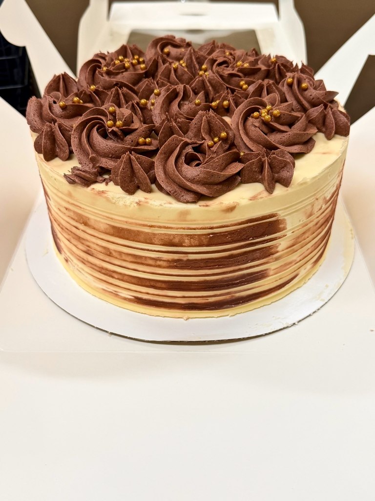 Cake with striped chocolate and vanilla sides, topped with chocolate rosettes and gold pearls
