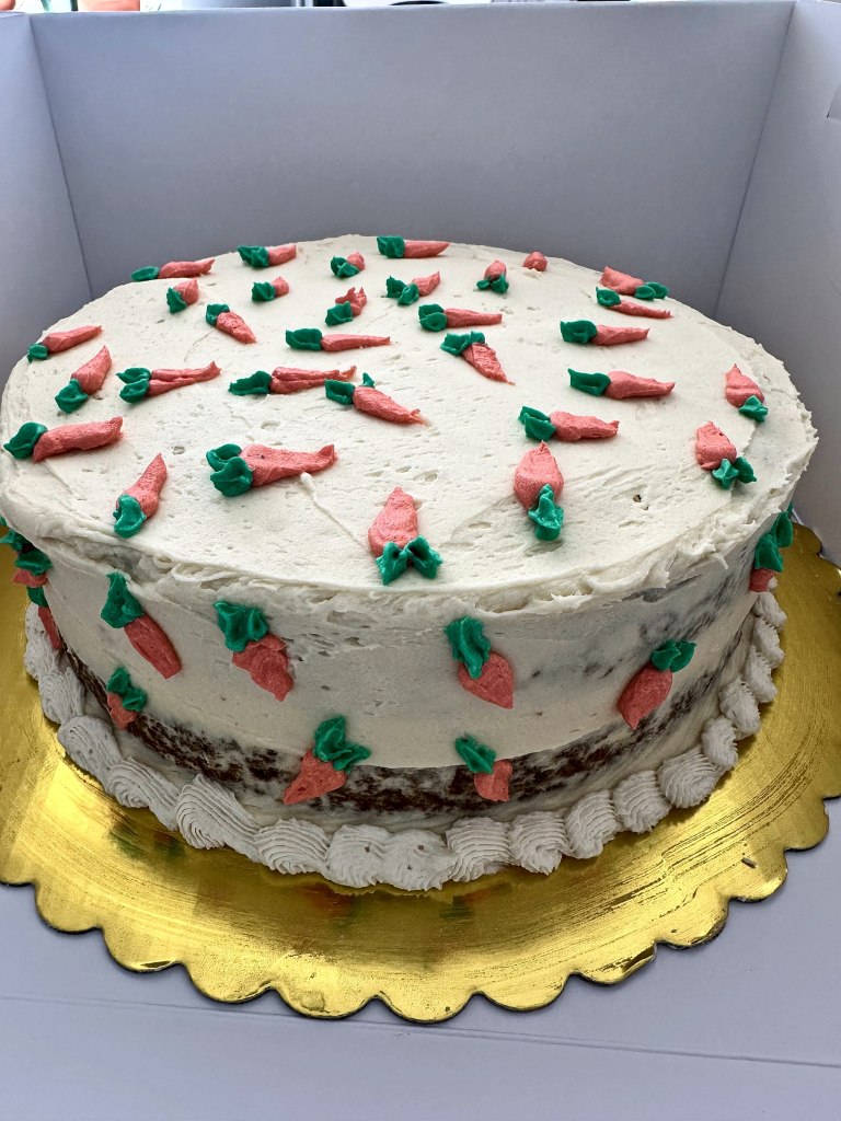 White frosted cake dotted with little frosting carrots on a gold board