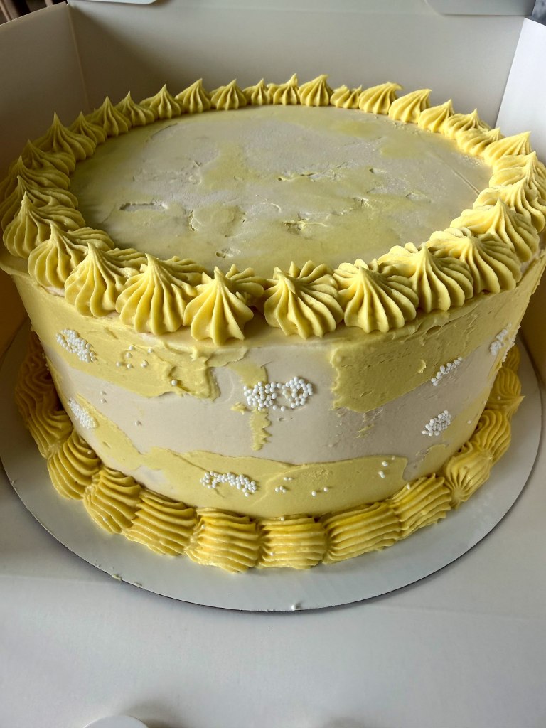 Pale yellow cake with bright yellow piped borders and white sprinkles
