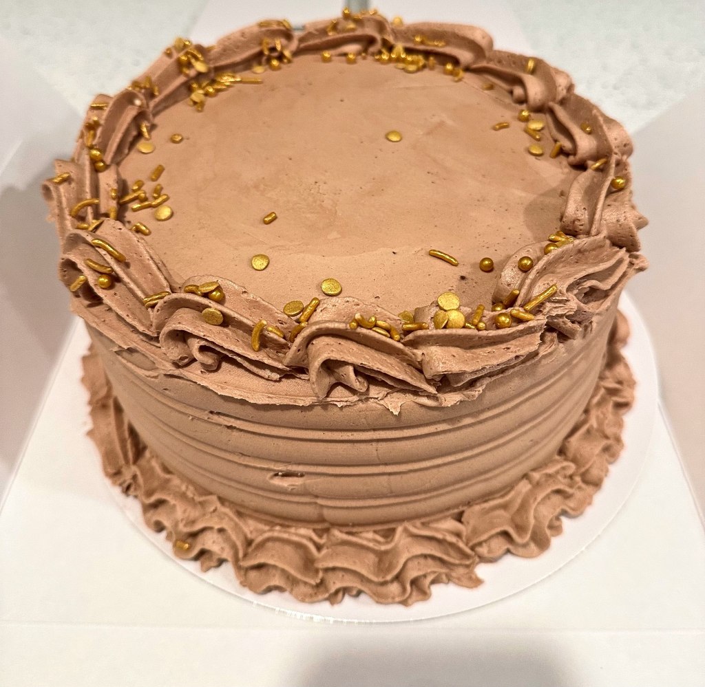 Chocolate frosted cake with piped borders and gold sprinkles