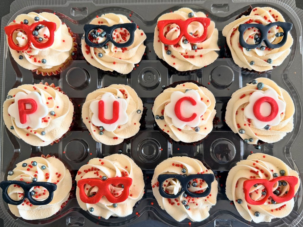 Cupcakes spelling PUCO between rows of red and black eyeglasses decorations
