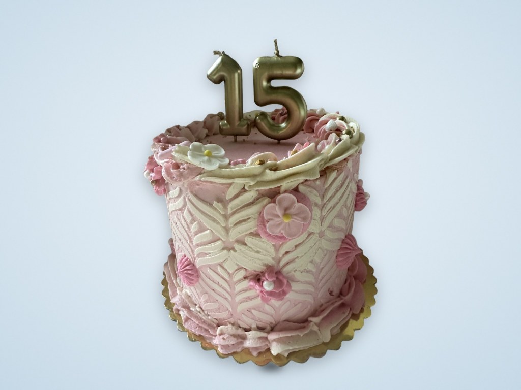 Pink and cream buttercream cake with sugar flowers and gold number 15 candles