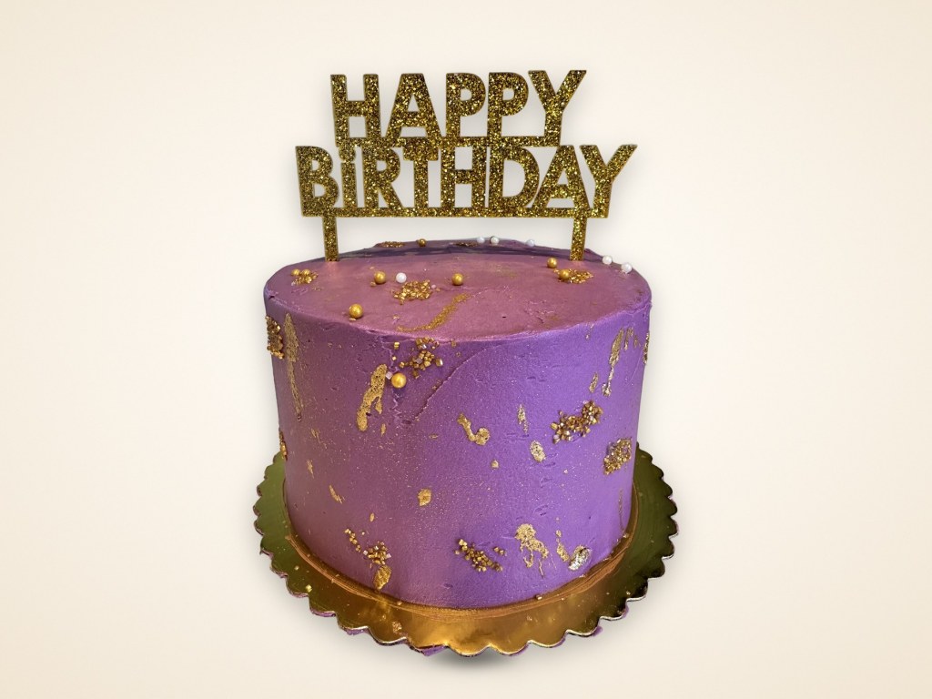 Purple buttercream birthday cake with gold flakes and a gold Happy Birthday topper