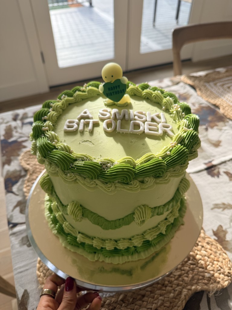 Green birthday cake with ruffled piping and pearls, A Smiski Bit Older lettering and a little Smiski figure holding a Happy Birthday heart